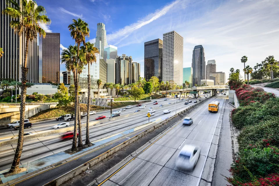 View of traffic on freeway with Los Angeles skyline and palm trees in background